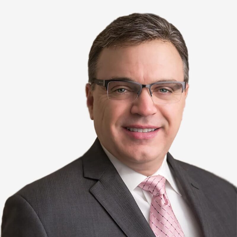 Smiling man in suit with glasses and pink tie.