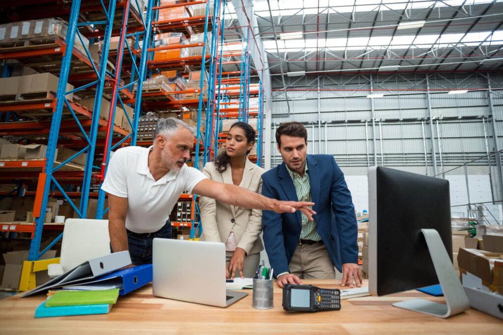 Warehouse managers and worker discussing with computer