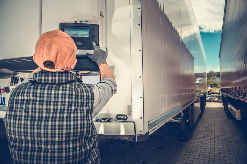 Worker adjusting temperature monitor on truck trailer.