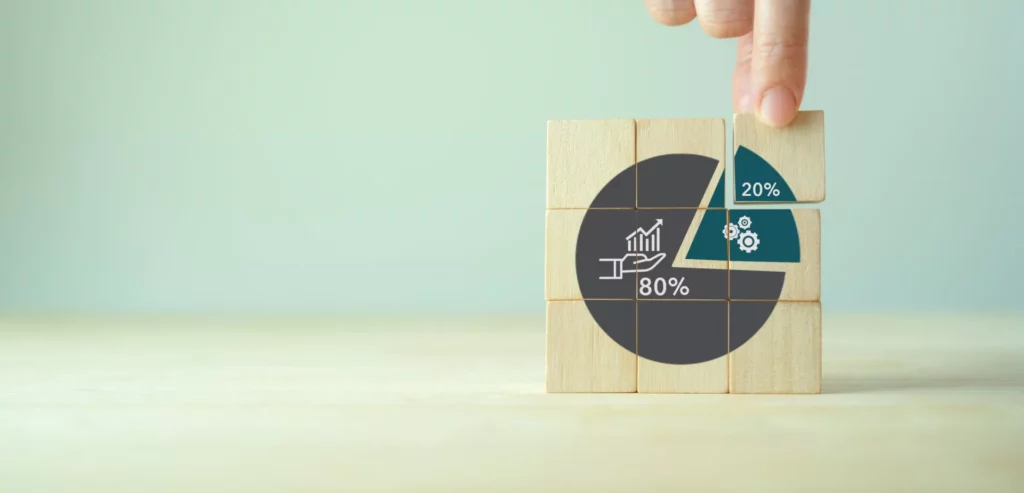 Hand placing a wooden block into a pie chart showing 80/20 distribution, representing business performance analytics and operational efficiency.