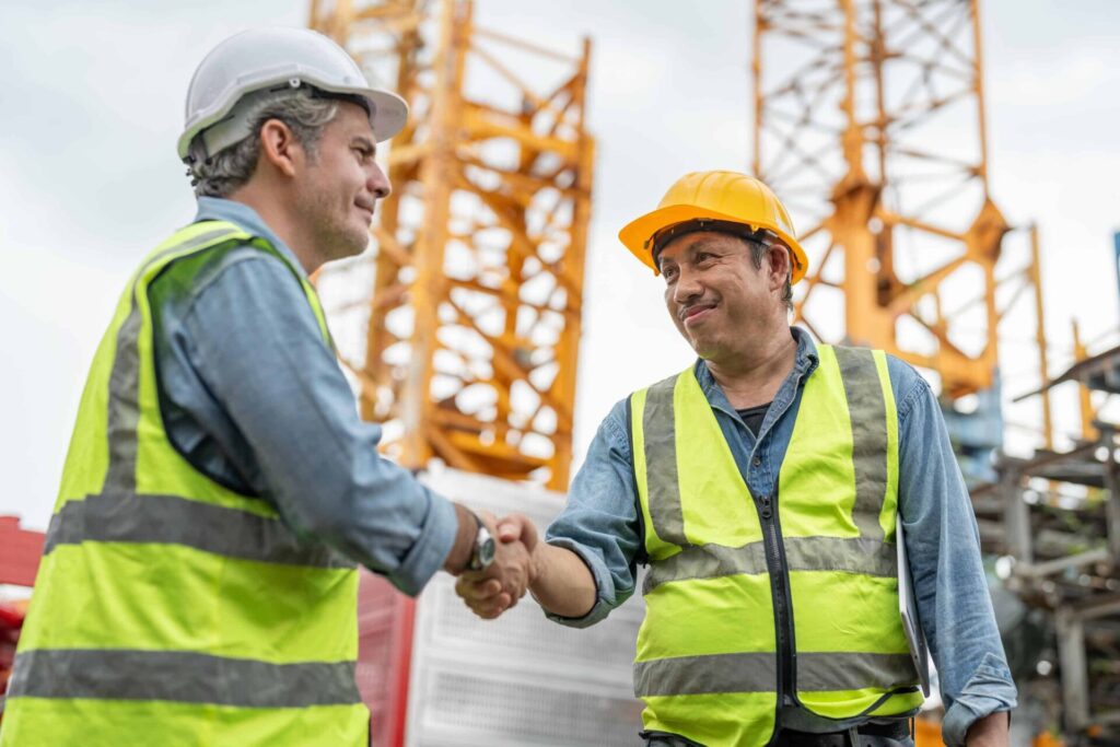 Two construction workers shaking hands on site.