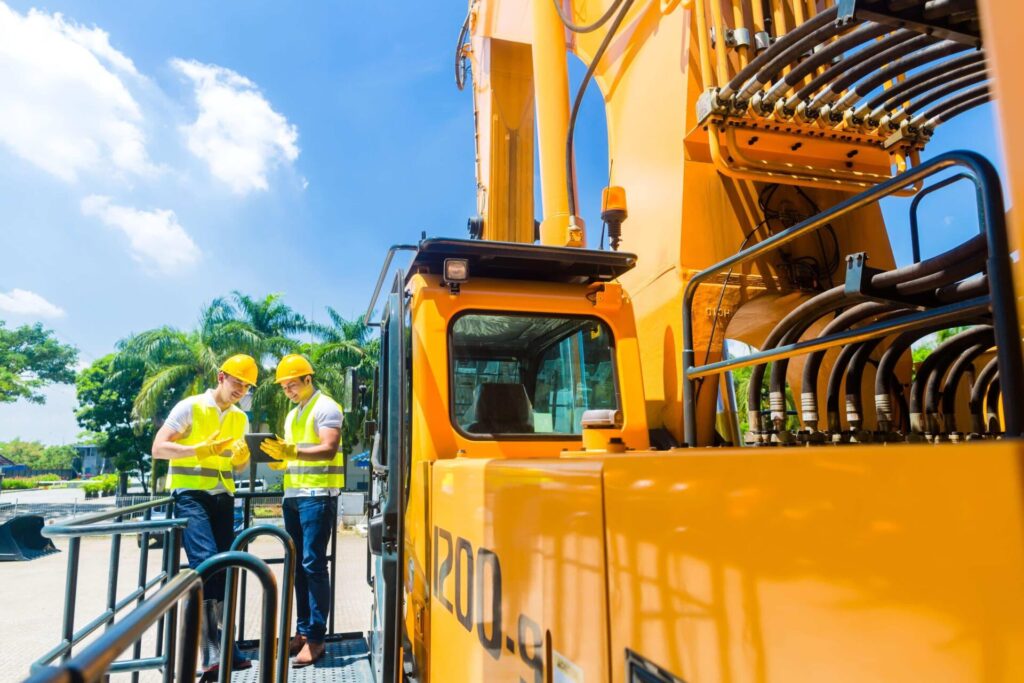 Construction workers discussing plans near heavy equipment.