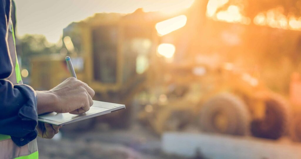 Construction worker writing on clipboard at sunset.