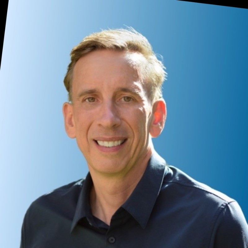 Smiling man with short hair against blue background.