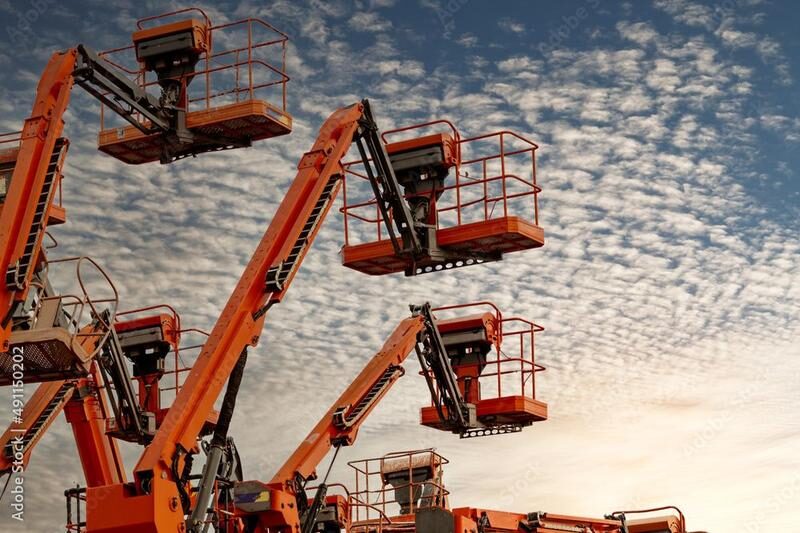 Multiple orange construction aerial lifts against cloudy sky.