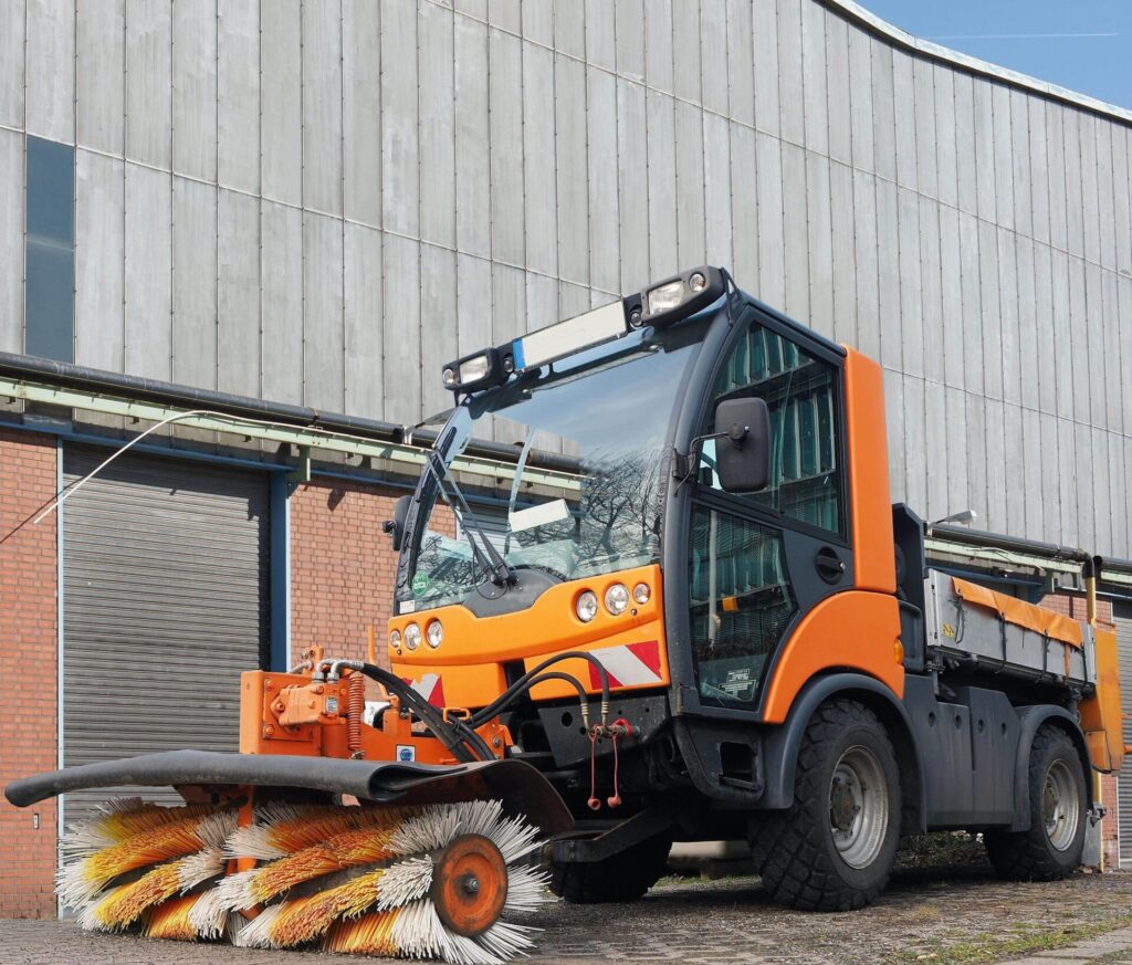 Orange street sweeper parked near a building.