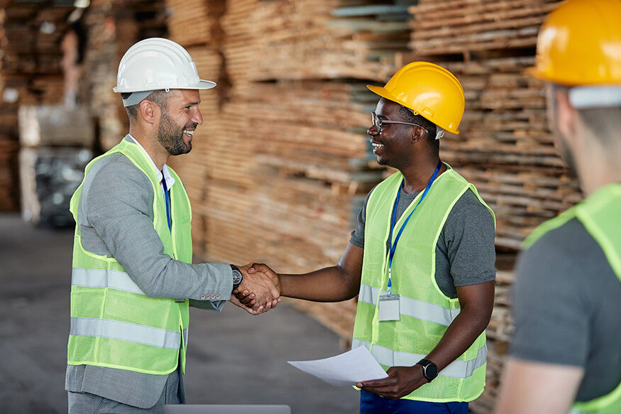 Two construction workers shaking hands in a warehouse.