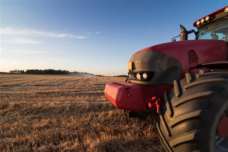 Red tractor on harvested wheat field at sunset